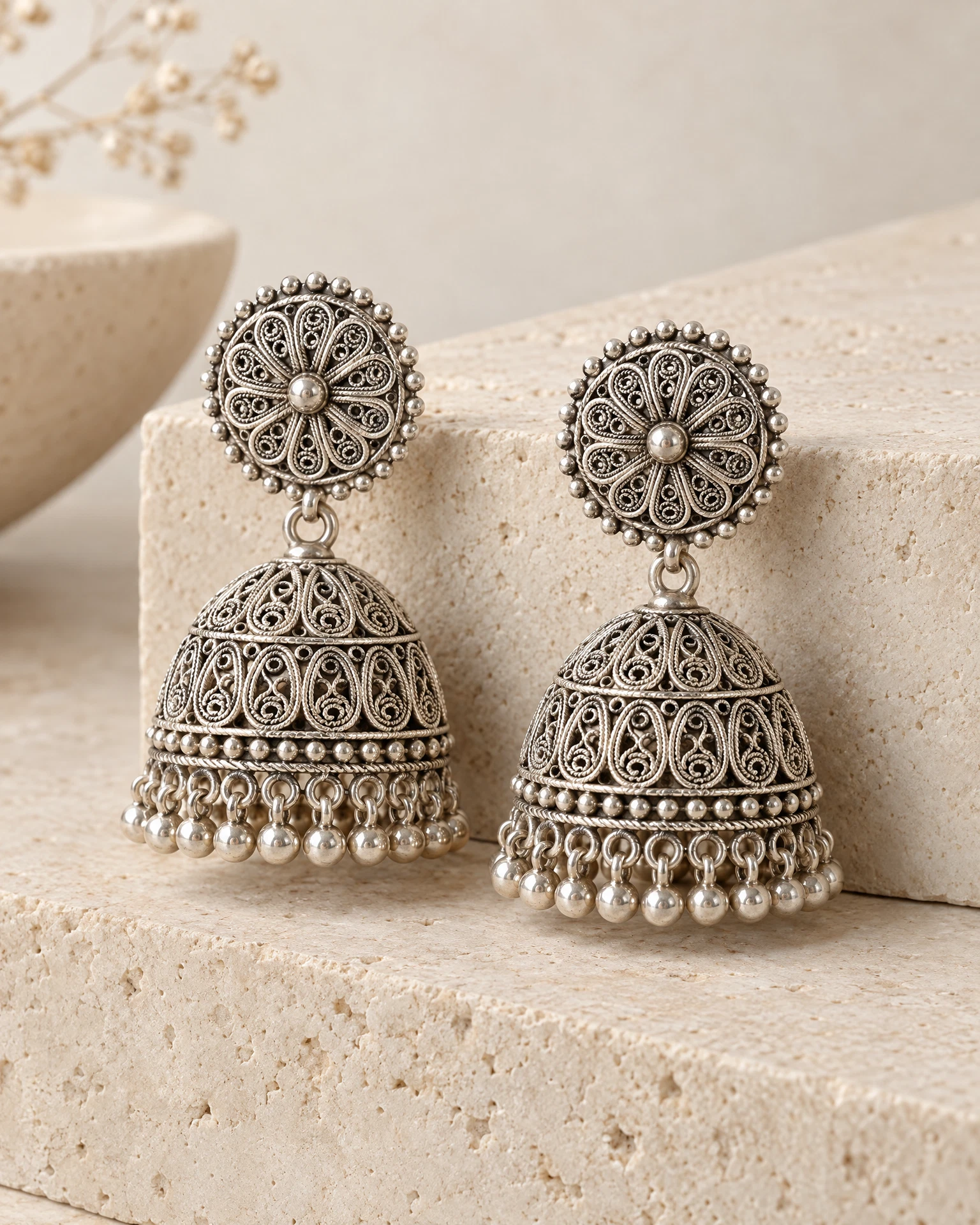 A pair of silver filigree jhumka earrings arranged on a pale stone display